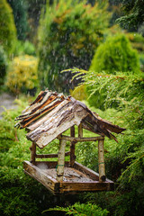 Wooden bird feeder in the garden during rain. Vertical.