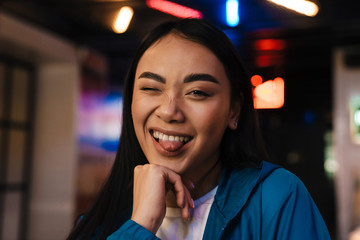 Photo of cheerful young asian woman grimacing and looking at camera