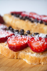 Peanut butter spread toasts with chocolate chips, strawberries, coconut flakes and homemade bread on a wooden plate