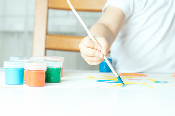 what to do for a child during the period of quarantine and self-isolation, child cook paints with a brush with blue paint on paper close-up, nearby are banks with colored gouache, creative background