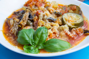 Vegetable stew with eggplant, zucchini, tomatoes and mushrooms. White plate and blue background