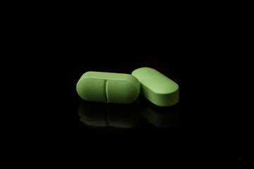 Two green pills are on a black table with a reflective surface.