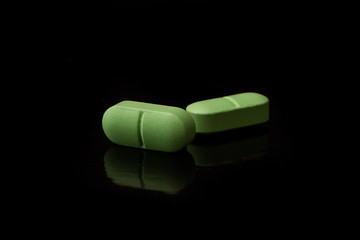 Two green pills are on a black table with a reflective surface.