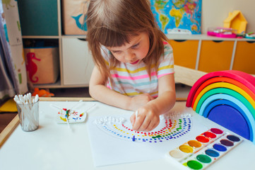 Adorable little girl painting dot rainbow using cotton sticks in the kids room