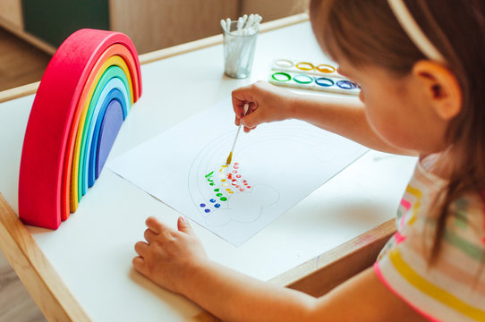 Adorable little girl painting dot rainbow using cotton sticks