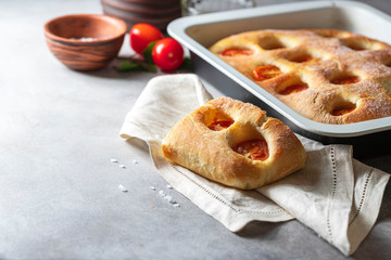 Italian bread focaccia with tomatoes and sea salt on grey concrete background. Homemade baking.