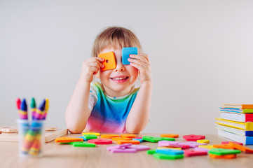 Happy little girl playing with colorful square shapes using it like eye glasses