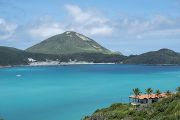 View of the beautiful lagoon with azure blue water and villa with red roofs on the coast among green trees, palms and bushes against the green mountains on a sunny day