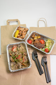 Paper bag and ready food in foil containers on a white background. Food delivery during the period of quarantine, self-isolation.