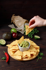 Hand dipping nachos in guacamole sauce on wooden table