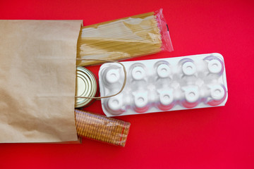 Paper bag with grocery food on a red background. Food delivery home during quarantine: noodles, canned food, buckwheat, crackers.