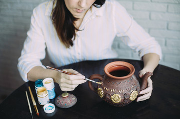 Girl artist paints a clay teapot in her workshop. Creativity. Handwork. Art. Self employment