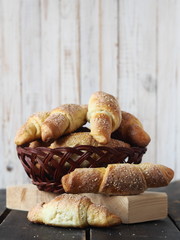 Croissants, sprinkled with sesame and sugar, in a natural vine plate on a dark wooden background.