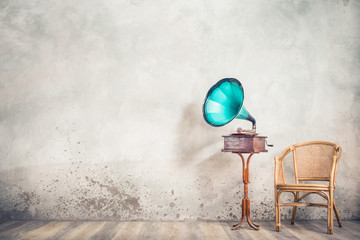 Vintage antique mint blue gramophone phonograph turntable from 20s on aged wooden stand and old rattan chair front loft concrete wall background. Nostalgic music concept. Retro style filtered photo