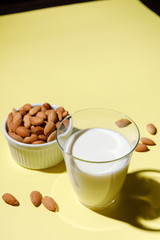 Almond milk in a glass on yellow background - alternative dairy