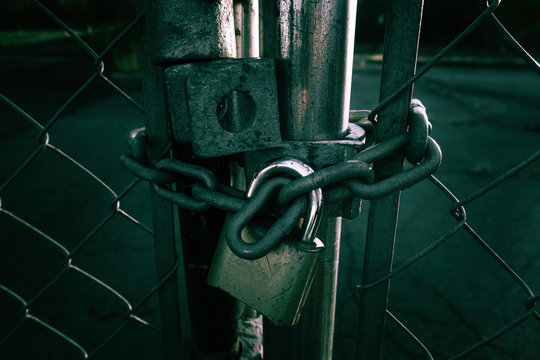 Locked Gate Tethered by metal chain and old rusty padlock on dark background.