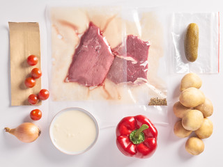 Delivery of packaged food for dinner. meat in plactic bag and vegetables: potatoes, onions, spices, cherry tomatoes, red pepper on white background