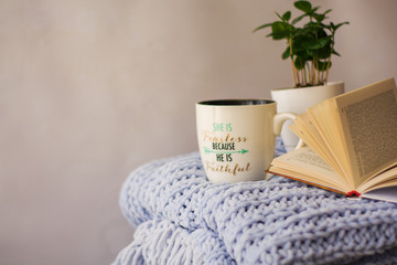Background of blue knitted plaid and pillows in cosy house with flower in pot and books, mug of tea, a garland. Home place work.