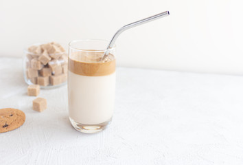Dalgona coffee delicious drink with whipped cream in a goblet with a metal straw and cane sugar in a jar on a light background.