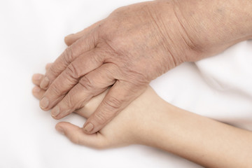 The hands of an old grandmother and a child touch in a handshake for support and help.