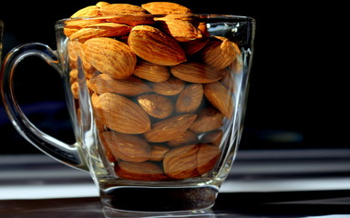 A closeup photo of a transparent glass cup filled with almonds.