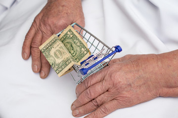 In the hands of a 90-year-old grandmother, an empty iron cart from a mini-store with one old dollar inside. Symbol of loneliness.