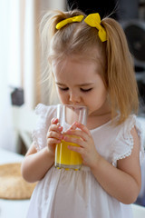 Little girl drinks fresh orange juice from a glass cup in the kitchen © Марина Гаращенко