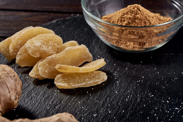 Slices of ginger dried fruit near which lies ground ginger in a plate and ginger root on a stone black plate. side view. Against viruses and diseases. immune product