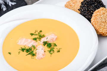 Cream soup with salmon in a white plate on dark concrete background