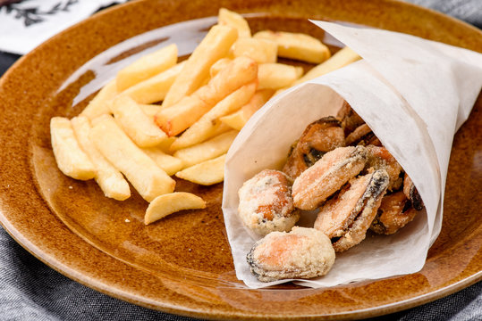 Mussel and french fries on a brown plate on a dark concrete background, decorated with fresh vegetables