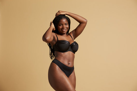 Curvy beautiful African American woman with braids in lingerie looking at camera against yellow background