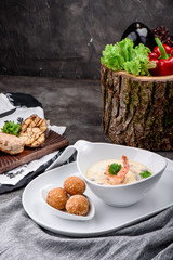 Cream soup with shrimps in white plate and plate with cheese balls on dark concrete background