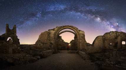 Back view of faceless traveler sightseeing remains of ancient castle under Milky Way at starry night
