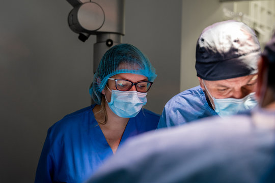 Pensive surgeon in uniform checking patient and making decision while coworker having consultation with colleagues during surgery in operating room of contemporary hospital