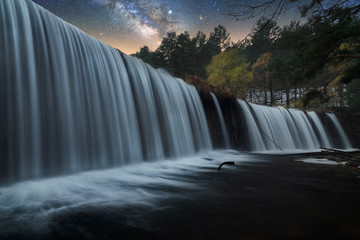 Beautiful powerful rocky waterfall and stream of water with colorful night starry sky on background