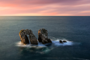 From above picturesque scenery of rough rocks among calm blue sea under colorful evening sky with sun beams breaking through clouds during twilight Costa Brava, Spain