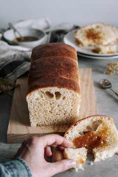 From above of crop hand taking piece of tasty Brioche bread with lam on table with loaf on wooden board in kitchen