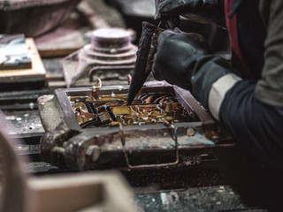 Side view from above of crop unrecognizable craftsman in black gloves using metal tools while pouring material in metal stencil in factory