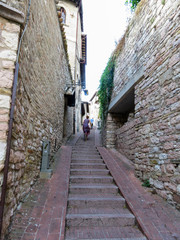 A young woman in a dress running up a stairs in a narrow street in the old town of Assisi, Italy