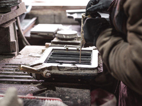 Side view from above of crop faceless male master in black gloves pouring material through cone to metal form for tiles in workshop