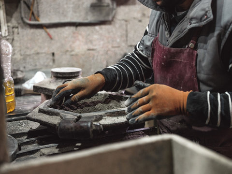Crop hand of faceless master in protection gloves removing metal heavy cover from shape with material for industry
