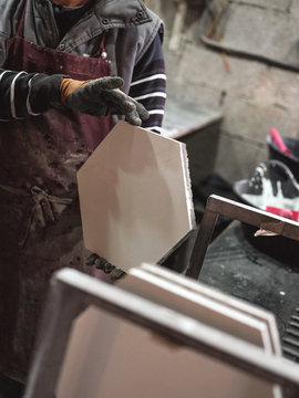 Crop male master in apron and gloves holding hexagonal fresh tile working with raw materials