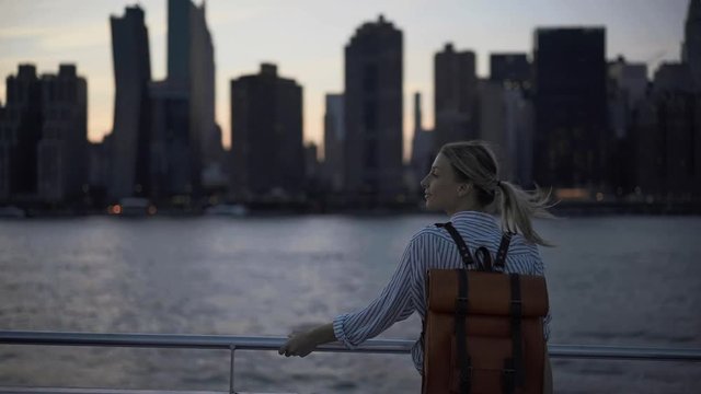 Young Caucasian tourist with trendy backpack enjoying voyage trip for exploring Manhattan island from water boat, amateur photographer using instant camera for taking pictures of New York
