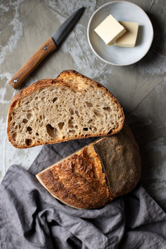 Cut half of delicious crispy sourdough bread loaf over wooden table with knife and butter