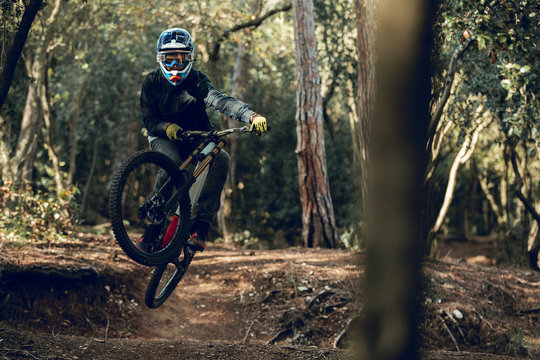 Unrecognizable man in helmet, gloves and protection glasses jumping doing whip trick downhill during mountain biking practice in wood forest