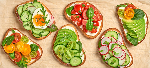 Italian vegan bruschetta on wooden board. Open sandwiches with avocado, cherry tomato, cucumber, radish. Various diet bruschetta with spinach, basil, top view. Flat lay, closeup