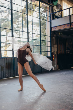 Unrecognizable young dramatic female dancer in black bodysuit performing sensual dance with tulle while training alone in light spacious studio