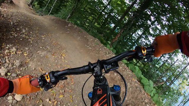 Point view biker hands on handle wheel while riding on bumpy berms trail road in summer forest. Cyclist holding handlebar riding in forest bike park. Exreme cycling on sport downhill mtb bicycle