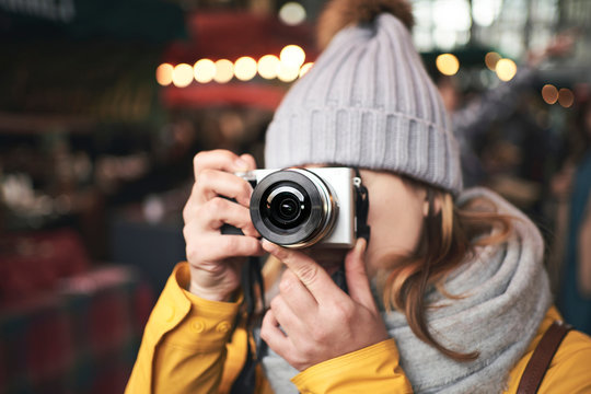 Unrecognizable female traveler in warm clothes taking pictures with camera while standing on city street with illumination in winter evening