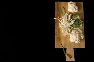 Wooden Board with cauliflower, cabbage and broccoli on a black background